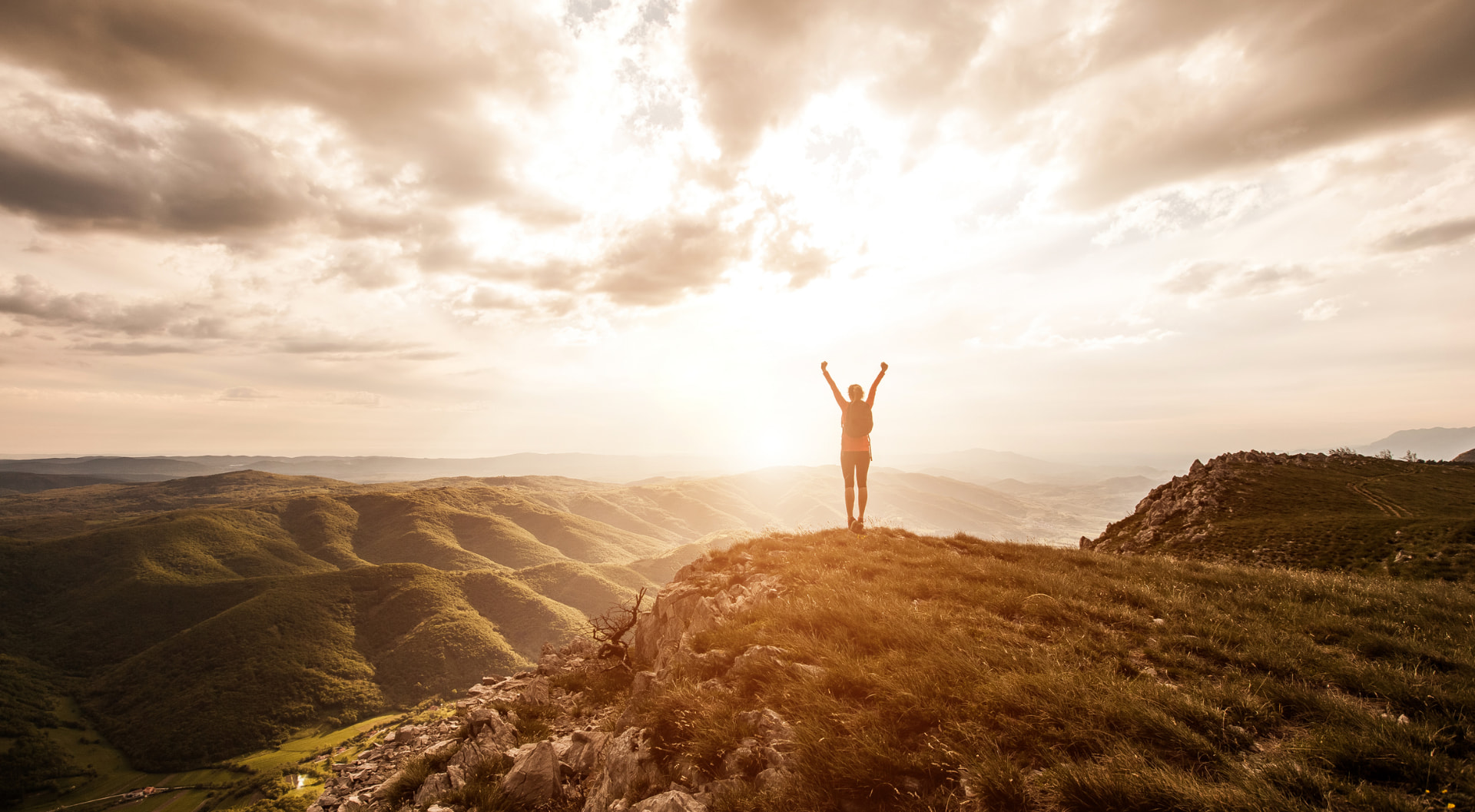 Person standing on a mountain ridge at sunrise with arms raised